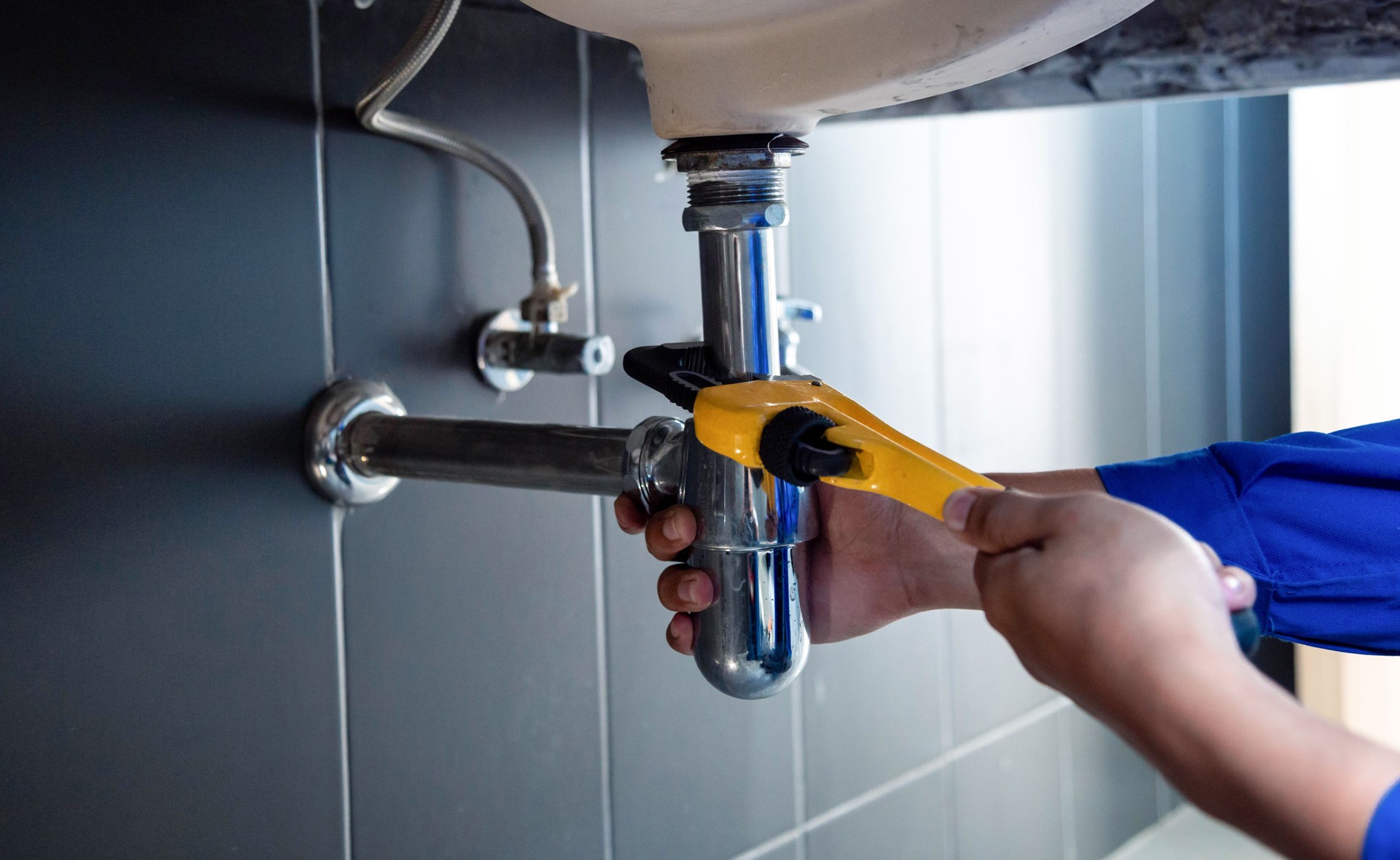 Plumber fixing sink pipe with adjustable wrench.